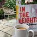 image of in the heights finding home with a full cop of coffee in front of a treelined backgroud with an umbrella and a bench.